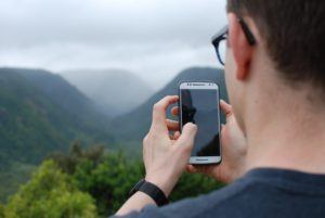 Young man in glasses holding cell phone while hiking,