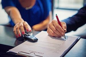 Woman signing auto loan with keys to new car.