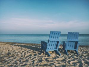 Two Adirondack chairs overlook a calm beach