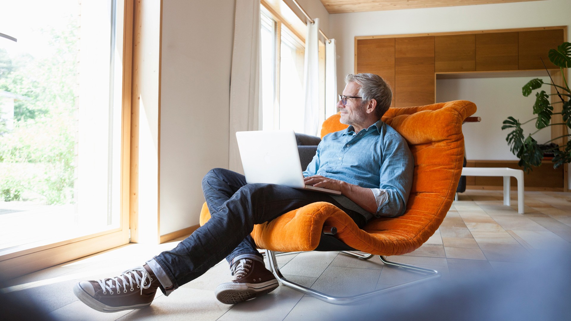 Mature man sitting on orange chair with laptop