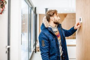 Man in winter coat adjusting thermostat