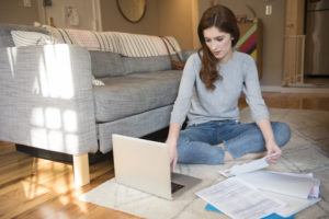 Woman sitting on floor paying bills with laptop