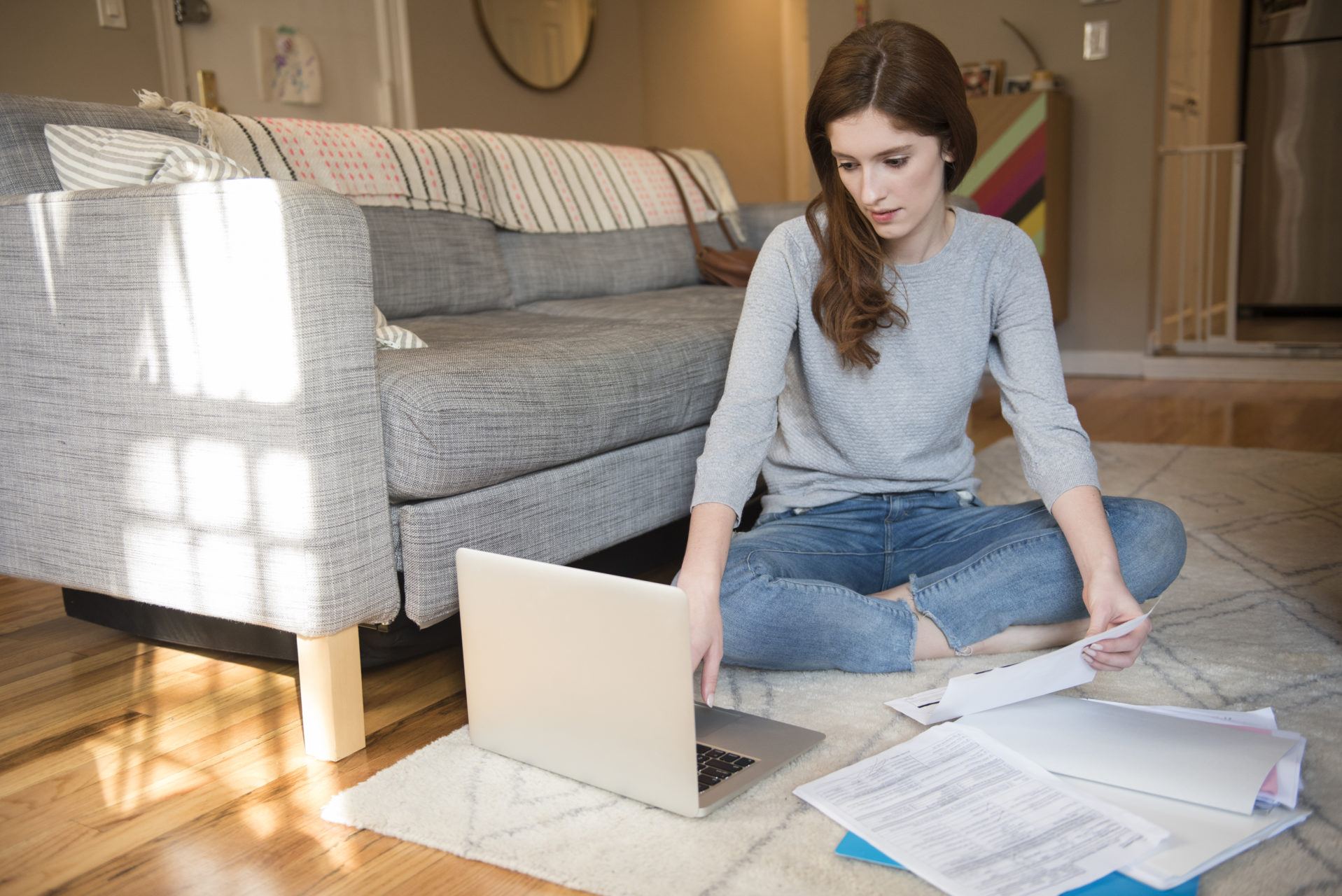 woman sitting on floor paying bills with laptop