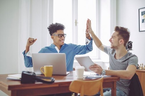 Two guys high fiving while sitting at table