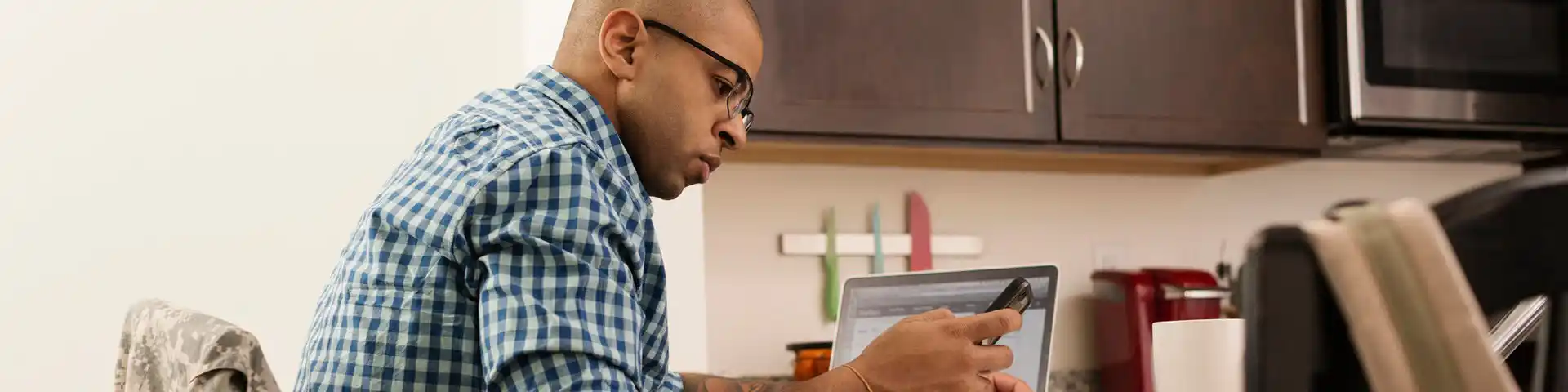man looking at his phone with his laptop next to him